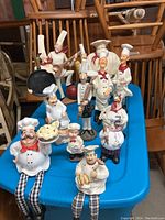 Full view showing all 13 resin chef figurines arranged on a blue table with varied poses and sizes