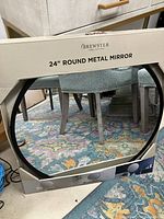 Boxed new 24 inch round black metal mirror by Brewster showing round shape and packaging.