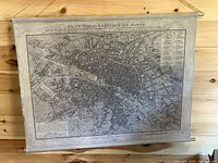 Full view of antique map reproduction of Paris on canvas with wooden roller edges and hanging string.