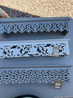 Top view of three carved wood shelves laid flat on table showing detailed carvings and tags with measurements.
