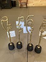 Four gold metal face sculptures on black pedestals arranged in a row.