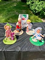 Five Annalee dolls arranged outdoors on black fabric including boxed lit kitty doll and four logo kids posed on individual felt bases