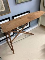 Side view of the antique wooden ironing board fully set up showing folding legs and overall shape.
