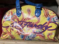 Front side of the bag with bright yellow background, peacock feather design and large Ed Hardy signature.
