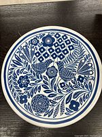 Front view of round ceramic folk art plate showing blue birds and floral pattern on white background.