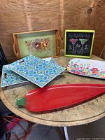 Overview of all six trays on wooden table showing chili pepper glass tray, floral wooden tray, margarita themed tray, floral and geometric patterned melamine trays.