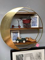 Front view of metal crescent moon shaped shelf with three wood shelves holding decorative items.