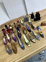 Photo showing 22 assorted miniature resin shoes and 5 small resin purses arranged on wooden floor.