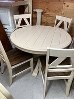 Full view of round pedestal table with four chairs around it. Table top is wood stained with cream painted base and chairs with stained seats and painted backs and legs.