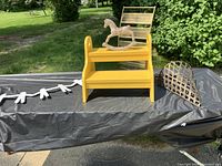 Yellow wooden two-step stepstool with side handles and a white wooden rocking horse on top, showing shape and color.