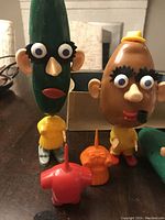 Photo showing front view of Cooky The Cucumber and Mr. Potato Head toys with several removable parts arranged in front and original box behind