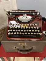 Front view of glossy red Underwood typewriter with white round keys, placed on brown case