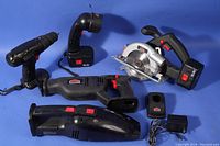 Photo showing all cordless power tools: drill/driver, reciprocating saw, circular saw, vacuum, light, charger, and batteries on blue backdrop.