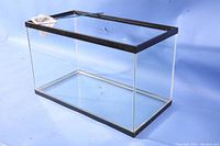 Glass aquarium empty on blue background showing clear panels and black frame.