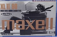 Box of Maxell XL II 90 high bias audio cassette tapes with packaging showing 10 pieces and advertising black magnetite technology.