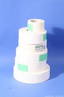 Stacked rolls of white drywall paper joint tape of varying widths forming a vertical column against a blue background.