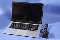 Silver laptop open with keyboard visible and black screen, power supply to the side.