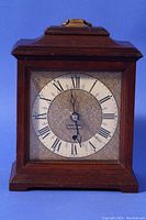 Front view of a square wooden mantle/desk clock with a white dial, Roman numerals, and second hand, marked Seth Thomas.