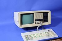 Front and side view of Olivetti M18P vintage PC clone with built-in CRT screen, dual floppy drives, keyboard, and cables on blue background.