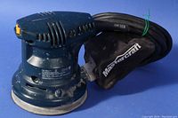 Mastercraft 5 inch random orbit sander with dust collection bag, showing side and top views. Power cord coiled and attached dust bag visible.