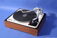 Full view of Garrard AT6 record player/changer showing tone arm, platter, and wooden base on blue background.