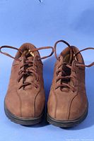 Pair of MBT men's brown leather shoes shown front and top sides with laces untied against blue background.