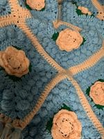 Close-up view of the crochet blanket showing the detailed blue textured squares and peach flower motif with green leaves.