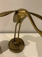 Side close-up of the brass crane statue showing details of wings, body, and circular base.