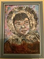 Full view of the framed vintage oil on board Inuit portrait painting showing the child's face, fur-lined hood, signature, and multicolor background.