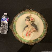 Full view of the framed portrait next to a water bottle for size reference. The circular frame has green decorative border and hanging chain at the top.