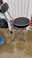 Single folding bar stool showing black cushioned seat and backrest with silver metal frame
