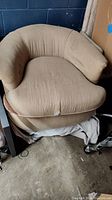 Front view of beige swivel chair showing tear on front seat cushion and curved armrests.