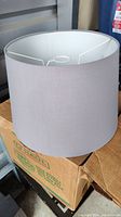 Light gray fabric lamp shade with internal metal frame shown sitting on stacked cardboard boxes.