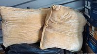 Two large beige fabric bed pillows together in storage, displayed at an angle showing their softness and thickness.