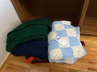 Stack of four folded handmade Afghan blankets showing a green blanket on top and a blue and white checkered blanket alongside.