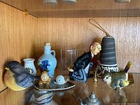 Photo showing clay hanging bell, butler statue, two bird figurines, miniature metal flowers, glass bud vase, pottery jug, ceramic vase, miniature carriage and snail on geode base.