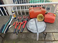 Full lot arranged on outdoor table including gas cans, lock bars, booster cable case, brushes, and spray cleaner.