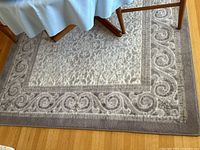 Close-up photo of the grey carpet showing decorative border and central pattern under a table.