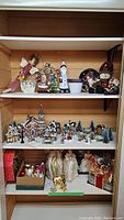 Shelf view showing assorted Christmas decorations including angels, snowmen, village scene, ornaments, and wreaths.