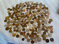 Wide image showing a large variety of coins spread on a fabric surface, illustrating the assortment and quantity of world coins.