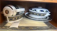 Set of Mikasa Arabella dishes stacked including cups, saucers, covered serving dish, plates, and trays with a blue and beige floral pattern