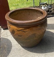 Side view of brown ceramic plant pot with raised dragon design outdoors on concrete patio showing detail.