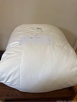 White king size feather duvet folded and stacked on a wooden surface. Label and note indicating 'King Duvet' visible.