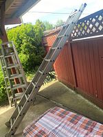 Full view of the 20-foot aluminum extension ladder standing outdoors next to a red fence, showing the ladder fully extended and resting on a covered patio area.