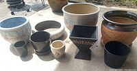 Nine assorted garden pots on concrete surface outside under daylight.