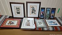 Nine indigenous framed art pieces arranged on a surface showing various styles and colors.