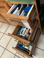 Photo of three wooden kitchen drawers filled with assorted kitchen utensils inside white plastic compartment organizers. Items include knives, scissors, peelers, and graters.