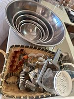 Overall view of 4 nested metal mixing bowls and woven basket with assorted cookie cutters and a small metal grater holder on kitchen countertop.
