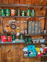 Shelves and bench area showing multiple green and red food cans filled with nails, screws, and bolts, plastic organizers with small hardware compartments, and boxes of lightbulbs and parts