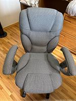 Front view of grey ergonomic office chair showing padded seat, backrest, and extendable armrests, placed on a wooden floor.